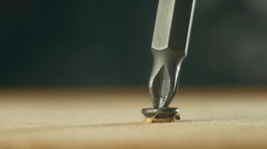 Yakın çekim tornavida, çelik tezgahın vidalarını sökerken tahta yüzeyden kendine dokunan vidayı ısırdı. Donanım aleti onarım sırasında başlıklı bağlayıcıyı kaldırıyor. İnşaat işinde çalışıyorum.