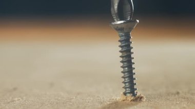 Yakın çekim tornavida vidası battı, tahta yüzeye vida battı. Tamir sırasında metal bağlayıcıyı sıkan donanım aleti. Yavaş yavaş inşaat işinde çalışıyorum.