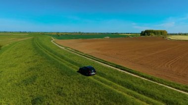 Ekin tarlaları arasında engebeli arazide SUV sürmek. İşlenmiş toprakları ayıran çimenlik yolda ilerleyen bir araç. Çiftlik arazisinin ortasındaki kırsal yolda giden bir araba.
