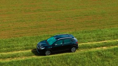 Çiftlik arazisinin yakınındaki çimenlik yolda hatchback araba sürüyorum. Düz olmayan çayır patikasının karşısında, tarlanın yanında seyir eden kompakt bir araç. Engebeli kırsal yol boyunca, küçük otomobil sürülen zeminin yanında ilerliyor.