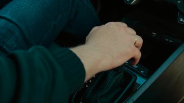Modern konforlu aile arabasıyla gezmek için otomatik vites değiştiren evli bir adamın eli. Parmaklar düzgün hareket ediyor, ileri hareket için şanzımanı çalıştırıyor. Sürücü vites değiştirme kipi, çağdaş sürüşe başlamaya hazırlanıyor