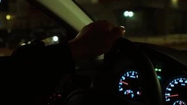 Geceleri şehirde tanınmayan bir adam araba kullanırken el ele tutuşan direksiyon. Erkek direksiyon, karanlık şehir caddesinde sürükleyici tekerlek. Gece sürüşü, loş bir ortamda el kontrollü direksiyon.