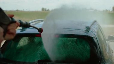 Otomobil yıkama servisinin çatısına su püskürten tanınmayan bir kadın. Dişi durulama aracı dışarıda yüksek basınçlı akış halinde. Güçlü su jeti kullanarak otomobilin üstünü temizleyen kişi