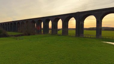 Tuğla viyadük gün batımında yemyeşil tarlaların üzerinde dimdik duruyordu. Büyük viyadük vadiden altın saatte geçiyor. Tarihi demiryolu köprüsü akşam ışığında canlı çayırların üzerinde yükseliyor.