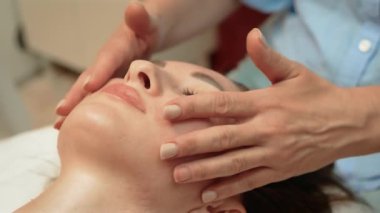 Güzellik salonunda yüz bakımı prosedürleri. Çekici müşteri yüz kozmetolojisi seansı alıyor. Kadın kafa ve yüz masajından zevk alıyor. Masa tedavisi prosedüründe yatıyor.