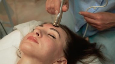 Premium Wellness Kliniği 'nde profesyonel yüz terapisi gören bir kadın. Elektrostimülasyon Cilt Gençleştirme, Yüksek Frekanslı Yüz Terapisi. Cilt arıtma, yüz gerdirme, yaşlı kadın için yaş azaltma terapisi, kozmetik uzmanı seansı.