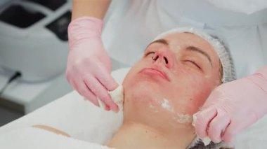 Cilt bakımı sırasında kozmetolojist müşterinin yüzünü siliyor. Profesyonel biri, nazikçe maskesini çıkarıyor. Tazeleyici ve temizleyici cilde odaklanan tedavi