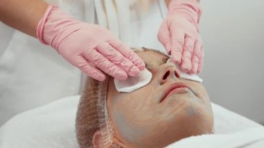 Yüz bakımı sırasında gelişmiş nemlendirici ve gençleştirme teknikleri deneyimi olan bir kadın. Güzellik uzmanı, rahatlamak için kadın gözlerine pamuk pedleri sürüyor. Hasta sakince uzanıyor, profesyonel cilt bakımının keyfini çıkarıyor.