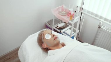 Kadın, sağlık merkezinde yüz bakımı yapmaktan zevk alıyor. Deri tedavisi sırasında göz rahatlığı için pamuk pedleri nazikçe yerleştirildi. Müşteri yenilenme ve gevşeme için özel bakım deneyimi yaşıyor
