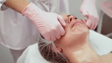 Estetisyen dikkatli bir yüz masajı yapıyor, hasta sakin. Dermatoloji bürosunun uzmanlığı tam olarak tedaviyi uygulamak, rahatlamayı sağlamak. Cilt bakımı profesyonel görünüş odaklı bakım ile