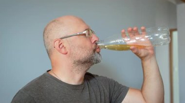 Yemek sırasında şişeden meyve suyu içen bir adam. Erkek, konteynırdan taze içkinin tadını çıkarıyor. Rahat bir ortamda rahatlamış ifadeyle bir yudum içen adam.