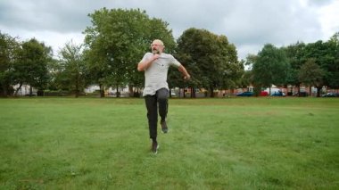 İngiltere 'de şehir parkında koşan komik bir adam. Yetişkin adam Britanya 'nın yeşil bölgesinde mizahi bir koşu yapıyor. Orta yaşlı bir adam, İngiltere 'nin eğlence bölgesinde komik bir ifadeyle koşuyor. Büyük Britanya 'da halk parkında oyuncu koşusu yapan adam.