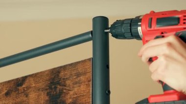 Elektrikli matkap kullanarak metal çubuğu dikey çerçeveye bağlayan adam. Erkek dayanıklı mobilyaları ev kullanımı için birleştiriyor. Endüstriyel stil rafında bağlantı kuran adam. Etkili kurulum için araçlarla çalışan teknisyen