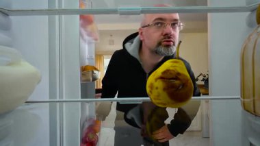 Buzdolabını açan, çürük armut bulan, onu koklayan ve iğrenerek yüzünü buruşturan bir adam, buzdolabının içinden manzara. Yetişkin bir erkek hayal kırıklığına uğrayıp iğreniyor. Bozuk meyveleri incelerken kötü kokuya tepki veriyor.