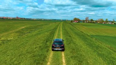 Kırsal arazileri ve kırsal bölgelerdeki ekin koşullarını incelerken kırsal kirleri araştıran komplike SUV. Resimli kırsal alandaki ekin tarlaları arasında yavaşça düz olmayan toprak yollarda giden araba. Sürücü mahsul yetiştirme durumunu denetliyor