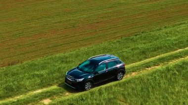 Tarım alanının yakınındaki dar çimenli yolda giden bir hatchback arabası. Çiftlik arazisinin yanındaki yeşil yolda ilerleyen kompakt bir araç. Küçük otomobil ekili toprağın yanındaki engebeli çayır yolunda ilerliyor.