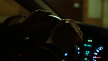 Geceleri tanınmayan bir adam şehir caddesinde araba kullanırken eller direksiyonu sıkıca tutuyor. Erkek seyir aracı, hava karardıktan sonra şehirde direksiyon başında. Gece şehir manzarasında araba kullanmak, aydınlık yol boyunca direksiyon sallamak.