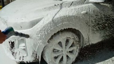 Benzin istasyonunda yüksek basınçlı köpükle araba yıkayan tanınmayan bir kadın. Dışarıdaki temizlik aracı için aktif sabun spreyi kullanan bir kadın. Araba gövdesinden toprak çıkarmak için basınçlı köpük uygulayan kişi