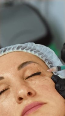 Kozmetik uzmanı, kırışıklıkları ve dikey yönelimi düzeltmek için göz kenarındaki dolguyu enjekte ediyor. Estetik uzmanı hassas göz altında yaşlanma karşıtı tedavi uyguluyor. Güzellik terapisti hyaluronik asit enjekte ediyor.