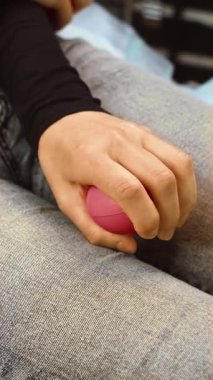 Squeezing heart shaped stress ball during facial injections in cosmetology clinic, vertical orientation. Holding pink anti stress toy for comfort while undergoing aesthetic procedure. Pressing stress relief object in hand to ease tension during