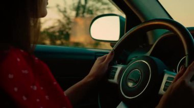 Gün batımında direksiyon başında araba süren bir kadın parlayan manzaraya bakıyor. Kadın direksiyon sakin yollarda ilerlerken gün batımını seyrediyor. Bayan gün batımında sakin manzaranın tadını çıkarıyor.