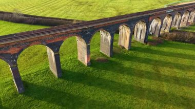 Altın saat ışığı ikonik İngiliz demiryolu viyaoluğunu kucaklıyor. Arka planda vadi ve tepeler olan demiryolu viyaoluğunun çarpıcı görüntüsü. Tanınmış yerler, iyi bilinen bölge, doğa manzarası boyunca ulaşım yolu.