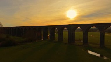 Altın gün batımına karşı dimdik duran tuğla viyadük. Welland Viyadük yumuşak günbatımı tonlarıyla yıkandı. Gökyüzü altında uzanan tarihi yükseltilmiş köprü.