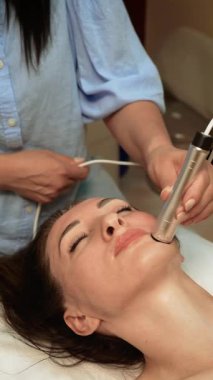 Güzellik uzmanı çeneye mikroakım kaldırma tedavisi uyguluyor, dikey yönelim. Cilt bakımı uzmanı yüz kaslarını geliştirmek için düşük seviyeli elektrik akımı kullanıyor. Estetik uzmanı, Ultrason Güzellik Terapisi ile cilt sertliğini arttırıyor.