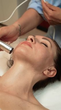 Çene üzerinde Darsonval Tedavi uygulayan estetik uzmanı, dikey yönelim. Cilt bakımı profesyonelce dolaşım ve kolajeni arttırmak için yüksek frekanslı akımlar kullanıyor. Güzellik uzmanı cilt dokusunu ultrasonik cilt sıkılaştırma sırasında inceliyor