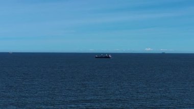 Kargo gemisi parlak gökyüzünün altında sakin bir şekilde yol alıyor. Ufukta dağılmış bulutlarla açık okyanusta ilerleyen bir yük gemisi. Sükûnetli sularda seyir halindeki ticari gemi ve etrafındaki uzak gemiler.