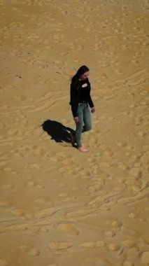 Kumsalda yürüyen bir kadın veya çöl, dikey oryantasyon. Güneşli kum tepelerinde ya da kıyı şeridinde gezinen bir kadın. Kuru kumda ya da kıyıda hareket eden bir kadın.