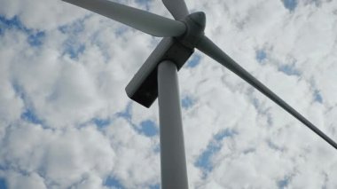 Bulutlu gökyüzüne karşı modern türbinle rüzgar enerjisi üretiyor. Dönen eko bıçaklar hava gücünü kullanıyor. Dönen yel değirmeni yenilenebilir elektrik üretiyor