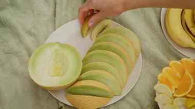 Elle dilimlenmiş kivi ve kavun hazırlıyorum. Sunum için meyve parçalarını düzgünce yerleştiriyorum. Servis için taze meyve tabağı hazırlıyorum.