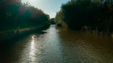 Kanal yemyeşil sularda sessizce süzülüyor. Su, açık gökyüzünün altında güneş ışığını yansıtıyor. Huzurlu İngiliz suyolu boyunca uzanan ağaçlar. Yaz öğleden sonra sakin kırsal bölge