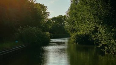 Kanal, yeşil gölgeli tekne rotasından geçiyor. Su, tekne açısından güneşli gökyüzünün altında sessizce süzülüyordu. İngiltere 'nin kırsal kesimindeki sakin sularda kavis çizen ağaçlar. Huzurlu İngiliz topraklarında huzurlu bir gezinti