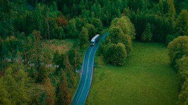Kamyon yağmurdan sonra virajlı orman yolunda gidiyor. Bulutlu gökyüzünün altında ıslak virajlı otoyol boyunca ilerleyen beyaz kamyonet. Ağaçlar ve açık yeşillikler arasında kaygan asfalt yolda giden bir kamyon.