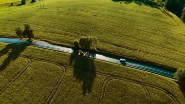 Islak kırsal yol boyunca araba sürüyor. Beyaz SUV, akşam güneşinin altında hareket ediyor. Altın yeşil alanlar arasında yolculuk yapan bir nakliye gemisi. Kırsal alanda seyahat eden bir makine