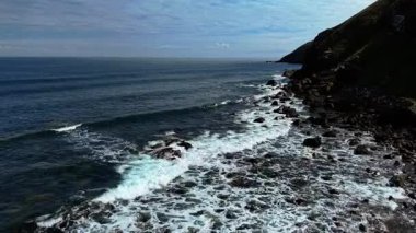 Dalgalar İskoçya 'da Kuzey Denizi' nin engebeli kıyı şeridine çarpıyor. Dalgalar dik kıyı boyunca koyu kayaları dövüyor. Çimenli kayalıkların etrafında köpükler uçuşuyor. Bulutlu gökyüzünün altında kıyı kayalarını parçalayan gelgitler