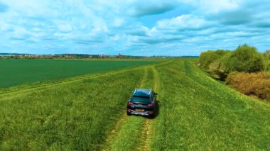 Tarımsal denetim için tarlalar arasında engebeli toprak yollar boyunca kırsal arazide gezinen araba. Araba kırsal alandaki çimenli patikalarda yavaşça ilerliyor, ekin büyümesini denetlerken, engebeli arazide ve tarlada manevra yaparken,