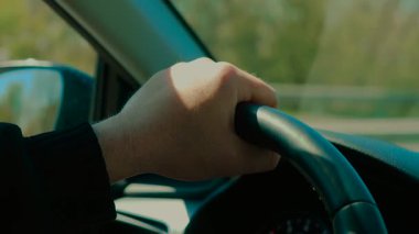 Tanımlanamayan bir adam otoyolda araba kullanırken direksiyonu sıkıca tutmak. Erkek kontrol aracı, gündüz sürüşü sırasında direksiyon başında. Sürücü aracı, yolculuk boyunca sıkıca dinleniyor.