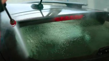Kadın, oto yıkamada arabanın arka camına yüksek basınçlı su püskürtüyor. Dişi, arka camları durulamak için güçlü su akıntısı kullanıyor. Aracın arka camını basınçlı jetle temizleyen kişi