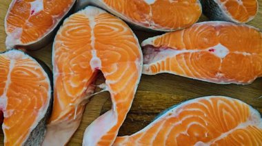 Tahta yüzeyde duran balık biftekleri. Somon kesikleri mutfak tahtasında dinleniyor. Çiğ deniz ürünleri dilimleri portakal dokusunu gösteriyor. Tezgahın üzerine yerleştirilmiş taze fileto parçaları