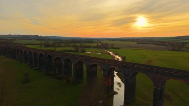 Akşam güneşinin sıcaklığını kucaklayan görkemli viyadük. Günbatımının sakin manzarası, tarihi viyadük vadisinden geçiyor. Tarihsel nokta, resim gibi doğa boyunca ulaşım sistemi.