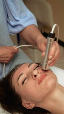 Yanakta Ultrasound Fat Redüksiyon uygulayan estetik uzmanlar, dikey yönelim. Cilt bakımı uzmanı yağ hücrelerini parçalamak için ultrasonik dalgaları kullanıyor. Seans sırasında yüksek frekanslı yüz terapisi ile yüz hatlarını iyileştiren güzellik uzmanı.