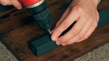 Elektrikli matkabı kullanarak, metal iskeleti ahşap zemine bağlayan adam. Erkek, ev tamiri için tornavidayla mobilya tamir ediyor. Adam iç geliştirme için raf montajı yapıyor.