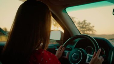 Gün batımında araba süren genç bir turist. Elinde direksiyon tutarken kırsal manzaranın tadını çıkarıyor. Kırmızı elbiseli kadın yeni yerler keşfediyor, altın ışık arabanın içini yansıtıyor. Gezgin sessiz yollarda geziniyor, güneş gibi yolculuğa odaklanıyor.