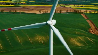 Tepedeki tarlaların yakınında türbinle rüzgar enerjisi üretiyor. Dönen bıçaklarla yeşil elektrik üretiyor. Dönen yel değirmeni kullanarak yenilenebilir enerji üretiliyor.