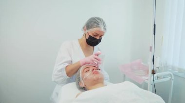 Kadın kozmetikçi, kız tenine gençleştirici tedavi uyguluyor. Kadın uzman, yüz bakımı için modern teknikler kullanıyor. Kız, cilt sağlığını ve görünüşünü iyileştirmek için tasarlandı