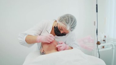 Profesyonel ortamda estetik estetik ameliyat yapan bir kadın. Parlak klinik aydınlatma altında yüz tedavisi için hassas aletler kullanan bir kadın. Cilt bakımı sırasında tedavi masasında uzanan kız