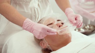 Kadın, şeffaf maske takarken yüz tedavisi görüyor. Maske dikkatlice yerleştirildiği için cilt bakımı sırasında kadın dinleniyor. Hidrasyon ve gençleştirme üzerine yoğunlaşarak güzellik bakım sürecinden geçen bir bayan.